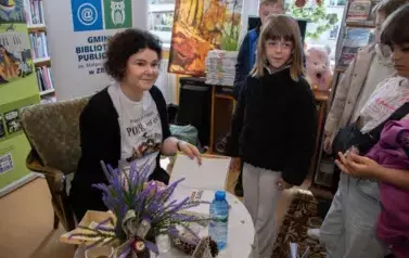 Anna Sakowicz przy stoliku podpisuje dedykacje na książce. Dzieci stoją obok Niej z zamiarem kupienia książeczki.