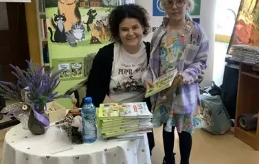 Przy stoliku Anny Sakowicz stoi dziewczynka z zakupioną książką. Kobieta przybliżyła się do dziewczynki i się uśmiecha.