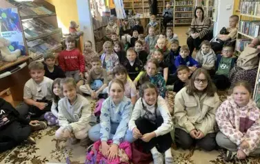 Duża grupa dzieci siedzi razem na dywanie w bibliotece.