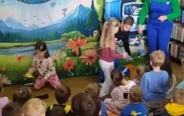 Z przodu jest troje dzieci, kt&oacute;re wrzucają śmieci do r&oacute;żnych kosz&oacute;w i aktorka w niebieskim kombinezonie.