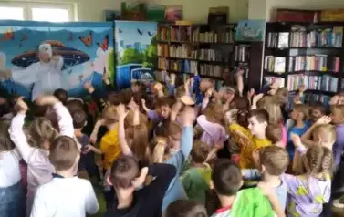 Z przodu aktor przebrany za białego misia pokazuje taniec z podniesionymi rękami, a dzieci z publiczności go nasladują i r&oacute;wnież tańczą.