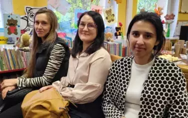 Trzy piękne Panie siedzą obok siebie i się uśmiechają.