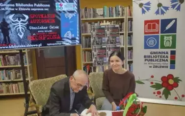 Obok Pana Ćwieka przy stoliku siedzi Czytelniczka czekając na wpis do nowo zakupionej książki.