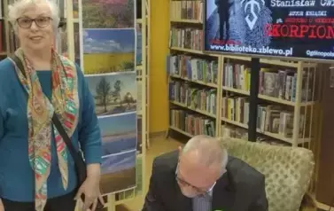 Starsza Pani w okularach stoi przy stoliku gdzie Pan Ćwiek podpisuje dedykację dla Niej na nowo zakupionej książce.