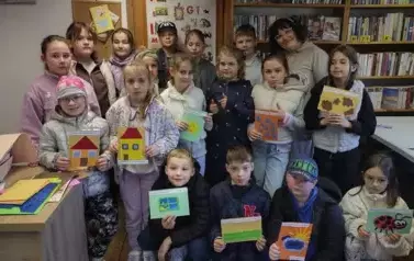 Dzieci stoją w grupie z Panią prowadzącą zajęcia. Trzymają w rękach swoje zrobione książeczki dotykowe.