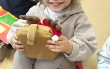 Uśmiechnięta dziewczynka w kitku trzyma pluszową książeczkę, obok widać inne dzieci bawiące się książeczkami.