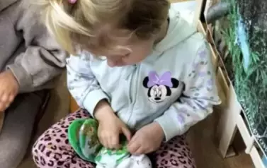 Dziewczynka w siwej bluzce i w kiteczku u g&oacute;ry przegląda pluszową książeczkę  z pieskiem. Obok widać chłopca.