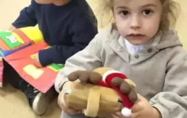  Dziewczynka w siwej bluzie trzyma pluszową książeczkę, obok widać chłopca kt&oacute;ry też ma pluszową książeczkę.