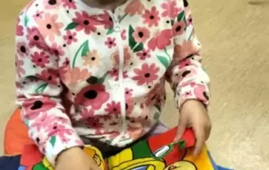 Dziewczynka w ciemnych włosach i bluzce w kwiatki bawi się książeczką pluszową o misiach.