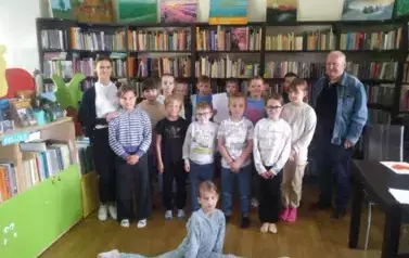 Dzieci stoją w grupie wraz ze swoją Panią i z Panem Wojtkiem, kt&oacute;ry gościnnie im czytał bajkę. Dziewczynka z przodu zrobiła szpagat.