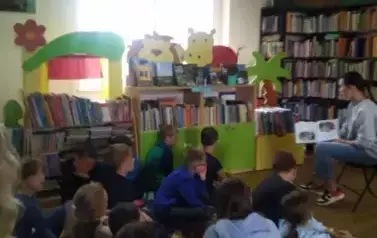 Dzieci siedzą na siedziskach i słuchają bajki, kt&oacute;rą czyta zaproszony gośc Nikola Sturmowska