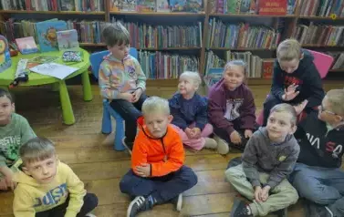 Dzieci siedzą na siedziskach i krzesełkach i słuchają bajki.