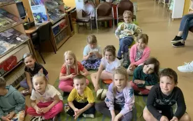 Dzieci siedzą na dywanie i słuchają bajki, kt&oacute;rą gościnnie czyta Pani Małgorzata Milewska