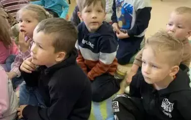 Dzieci siedzą na dywanie i słuchają bajki, kt&oacute;rą gościnnie czyta Pani Małgorzata Milewska