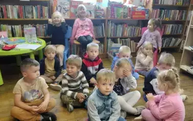 Dzieci siedzą na siedziskach i krzesełkach i słuchają bajki.