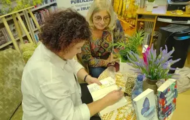Pisarka przy stoliku podpisuje książkę czytelniczce.