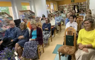 Wszystkie krzesła są zajęte przez gości. Ludzie patrzą z zaciekawieniem.