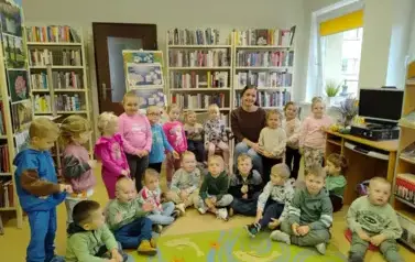 Dzieci siedzą w p&oacute;łkolu razem z bibliotekarką.