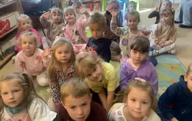Dzieci siedzą na dywanie i słuchają bajki.