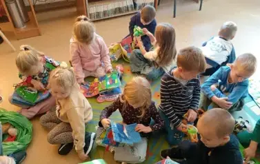 Dzieci siedzą na dywanie i bawią się pluszowymi książeczkami. 