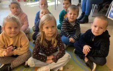 Dzieci siedzą na dywanie i słuchają bajki.