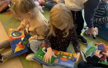 Dzieci siedzą na dywanie i przeglądają pluszowe książeczki.