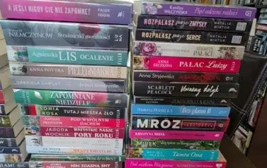 Na stole z bliska widoczne dwa rzędy nowych książek z widocznymi tytułami.
