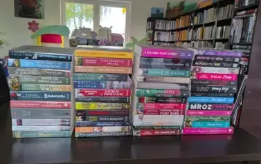 Na stole w czterech rzędach są ułożone pionowo nowe książki z widocznymi tytułami.