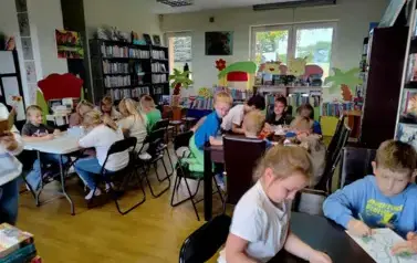 Dzieci przy trzech stołach kolorują na kartkach smoki.
