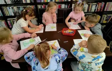 Przy stole siedzą dzieci i kolorują smoki.