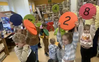 Dzieci stoją i trzymają w g&oacute;rze siedziska z numerkami. widać numerki 2,4,8