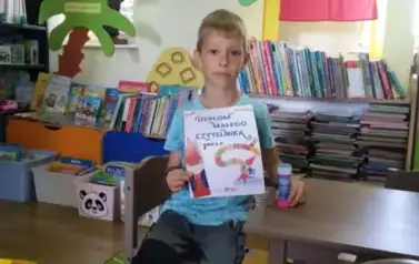 Chłopiec w blond włosach siedzi przy stoliku w bibliotece w Pinczynie i pokazuje sw&oacute;j dyplom Małego Czytelnika.