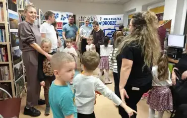 Dzieci stoją w k&oacute;łeczku wraz ze swoimi rodzicami i z Panią z biblioteki.