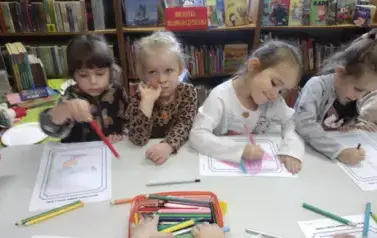 Dzieci przy stole malują kredkami na kartkach swoich ulubionych bohater&oacute;w z bajki.