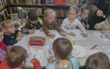 Dzieci przy stole malują kredkami na kartkach swoich ulubionych bohater&oacute;w z bajki.