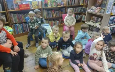 Dzieci siedzą na siedziskach w Borzechowie i słuchają bajki. Jeden chłopiec siedzi na kolanach u swojej Pani.