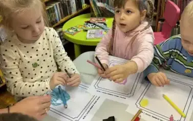 Dzieci siedzą przy stole i kredkami rysują na kartkach swoją ulubioną postać z bajki.