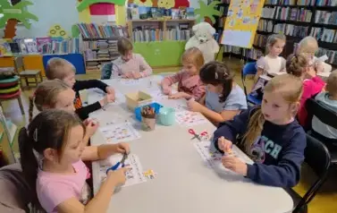 Dzieci siedzą przy stołach i naklejają w odpowiednie budki misie bawiąc się w misiowe sudoku.
