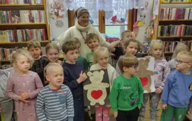 Wszystkie dzieci stoją w grupie razem z Panią Małgosią prowadzącą zajęcia. Dwoje z dzieci trzyma na kartkach wyklejone misie z serdusziem na brzuchu.