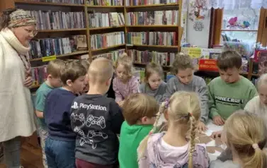 Pani Małgosia prowadząca zajęcia patrzy na dzieci kt&oacute;re przy stole wyklejają misie.