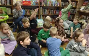 Dzieci siedzą na siedziskach, niekt&oacute;re z nich podnoszą rękę w celu zabrania glosu.