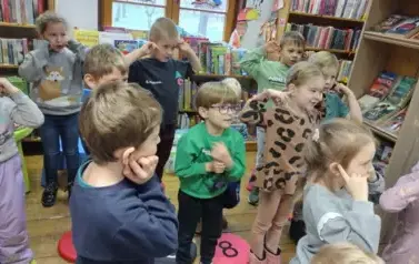 Dzieci stoją w rozsypce i palcami dotykają swoich uszu.