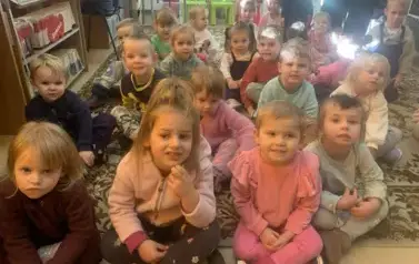 Dzieci siedzą na dywanie i się uśmiechają.