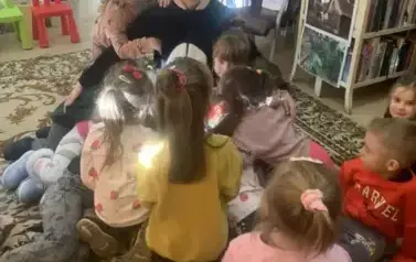 Dzieci siedzą na dywanie i przytulają się do kobiety przebranej za misia Pandę.