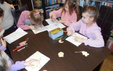 Dziewczynki siedzą przy stole i uzupełniają świąteczne karty pracy