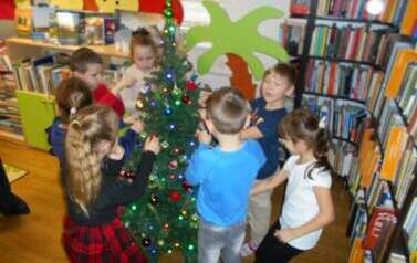 Siedmioro dzieci stoi przy choince i zawiesza dekoracje.