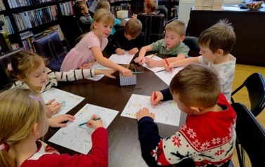 Dzieci siedzą przy dw&oacute;ch stołach i kolorują choinkę według podanego kodu