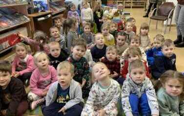 Duża grupa dzieci siedzi na dywanie i słucha bajki czytanej przez bibliotekarkę.