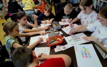 Dzieci siedzą przy stołach i niekt&oacute;re rozwiązują krzyż&oacute;wki,a inne uzupełniają matematyczne igloo kolorując kształty odpowiednim kolorem jaki pokazuje wynik z obliczeń.