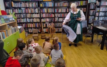 Dzieci siedzą na dywanie i patrzą na Panią Krysię, kt&oacute;ra pokazuje im części sp&oacute;dnicy kociewskiej